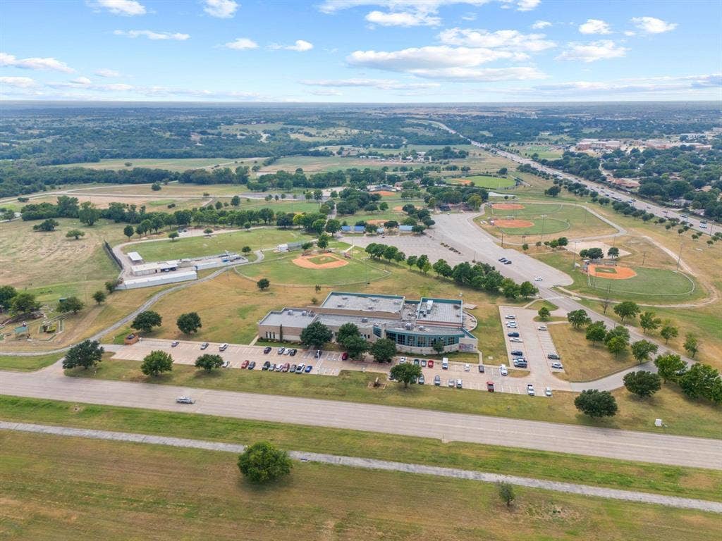 1205 Augusta Road, Benbrook, TX 76126 Expansive recreational facility featuring multiple baseball diamonds, a contemporary multi-story building, dedicated parking areas, and surrounding green spaces