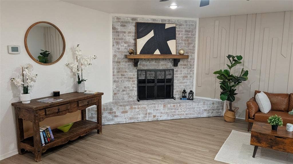 1205 Augusta Road, Benbrook, TX 76126 Whitewashed brick fireplace with a wood mantle and dark metal screen, complemented by plank-style flooring