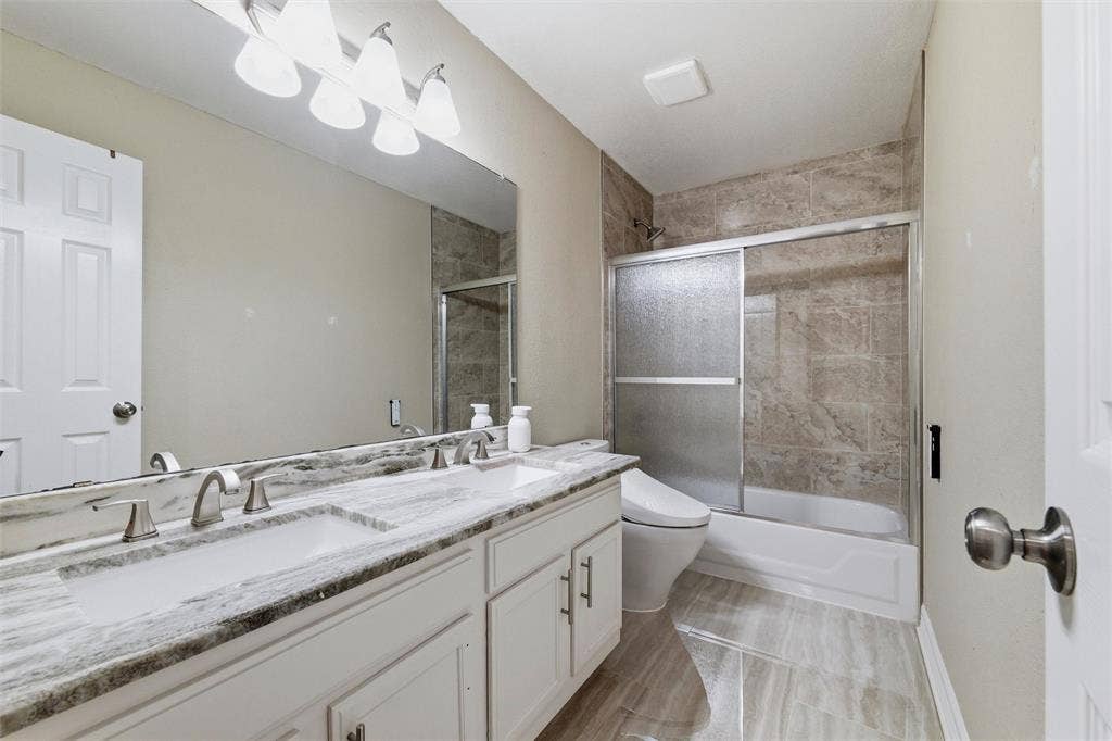 1432 Honey Locust Drive, Plano, TX 75023 Hall Bath Up with dual sinks, marble counters, floor and tub shower surround with glass enclosure, upgraded bidet commode.