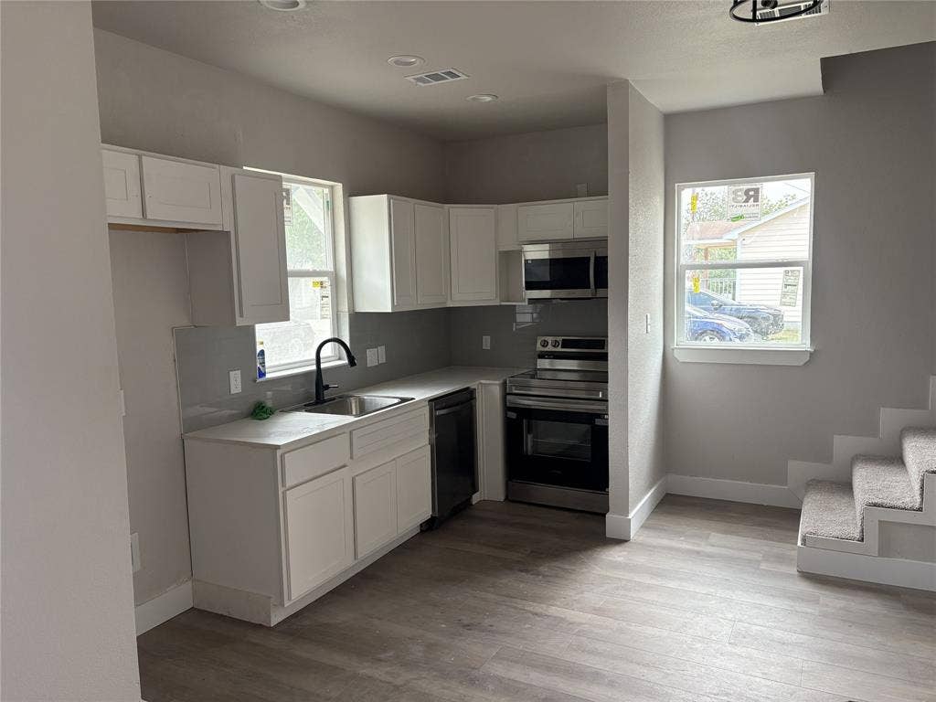316 Henry Street, Waxahachie, TX 75165 Modern kitchen featuring white cabinetry, light gray countertops, stainless steel appliances, a black gooseneck faucet, and wood-finish flooring