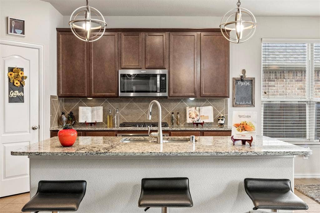 1437 Tanglewood Trail, Northlake, TX 76226 Kitchen featuring a granite-topped island with seating, dark wood cabinetry, stainless steel appliances, and a tile backsplash