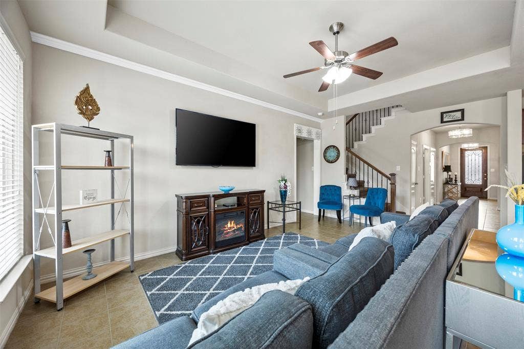 1437 Tanglewood Trail, Northlake, TX 76226 Open concept living space featuring tile flooring, crown molding, a ceiling fan with integrated lighting, and an elegant staircase with wood and wrought iron balusters