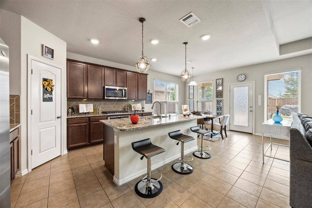 1437 Tanglewood Trail, Northlake, TX 76226 Kitchen featuring dark wood cabinetry, a granite-topped island with seating, stainless steel appliances, and tile flooring