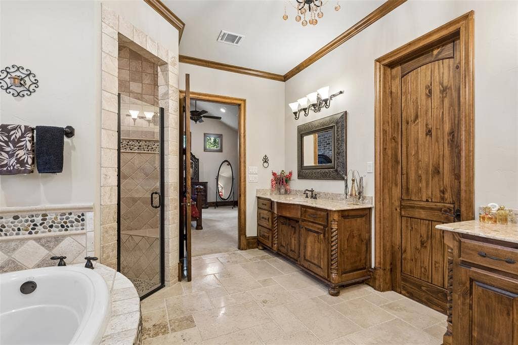 125 Audrey Drive, Keller, TX 76248 Primary bathroom featuring granite countertops, travertine flooring, chandelier, walk in closet, jetted soaking tub, walk in shower and makeup vanity.