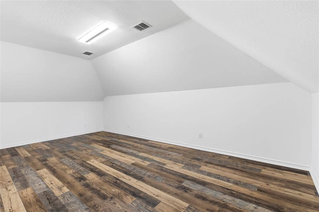 544 Hubbard Circle, Nevada, TX 75173 Spacious room featuring sloped ceilings, white walls, wood-finish flooring, and a flush-mount ceiling light fixture