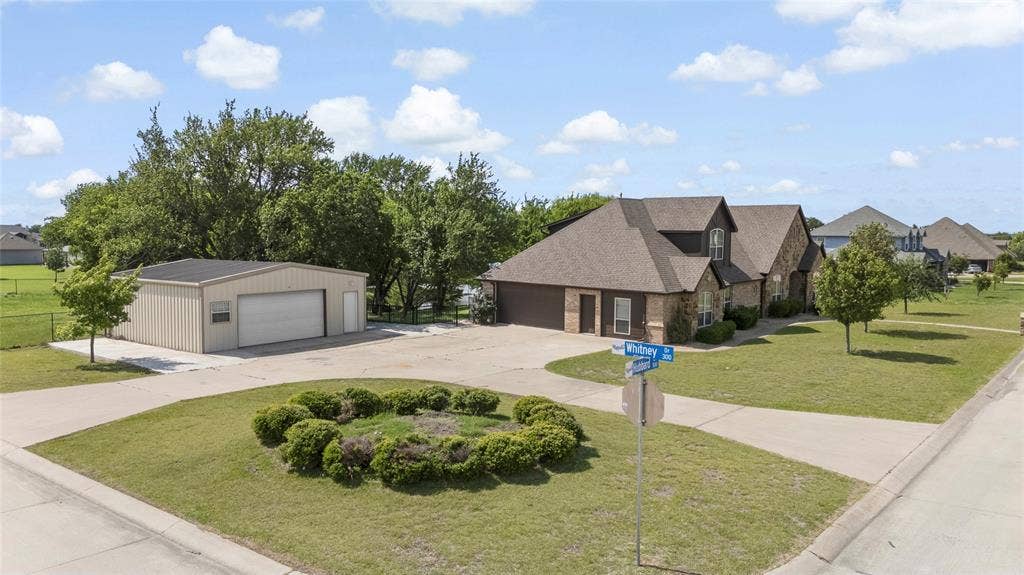 544 Hubbard Circle, Nevada, TX 75173 Spacious property featuring a brick and siding residence with a dark shingle roof, an attached two-car garage, and a separate large metal outbuilding with a roll-up door