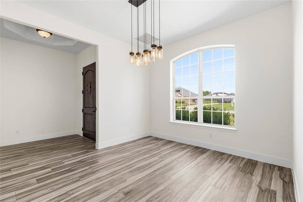 544 Hubbard Circle, Nevada, TX 75173 Spacious room featuring wood-finish flooring, a contemporary multi-bulb linear chandelier, and an arched window with grid panes