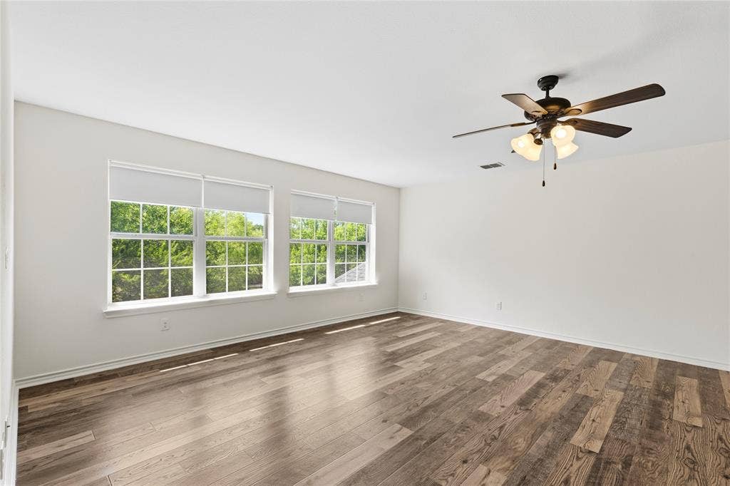 544 Hubbard Circle, Nevada, TX 75173 Spacious room featuring wood-finish flooring, multiple windows with roller shades, and a ceiling fan with integrated lighting