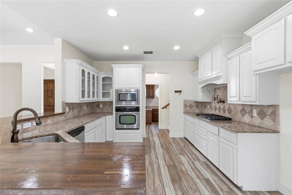 544 Hubbard Circle, Nevada, TX 75173 Open-concept kitchen featuring white shaker cabinetry, stainless steel appliances, granite countertops, a diamond-patterned tile backsplash, and wood-finish flooring