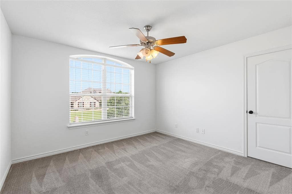 544 Hubbard Circle, Nevada, TX 75173 Spacious room featuring light gray patterned carpeting, a large arched window with horizontal blinds, and a ceiling fan with integrated lighting