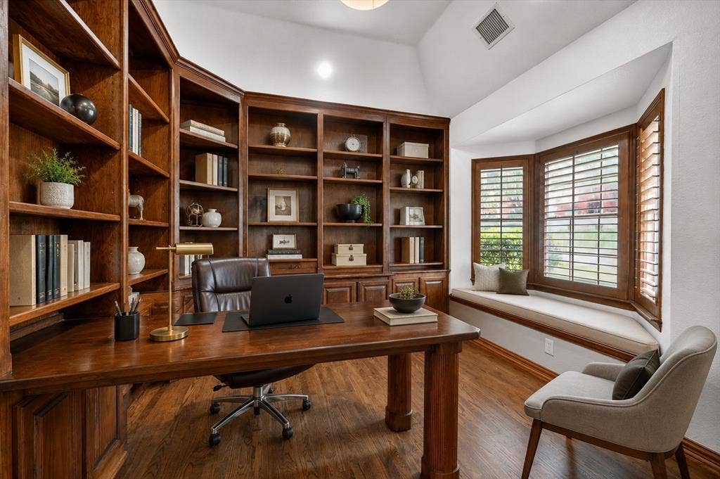 4437 Lone Tree Drive, Plano, TX 75093 Dedicated office space featuring extensive built-in wood bookcases, wood-finish flooring, a bay window with integrated seating, plantation shutters, and a vaulted ceiling