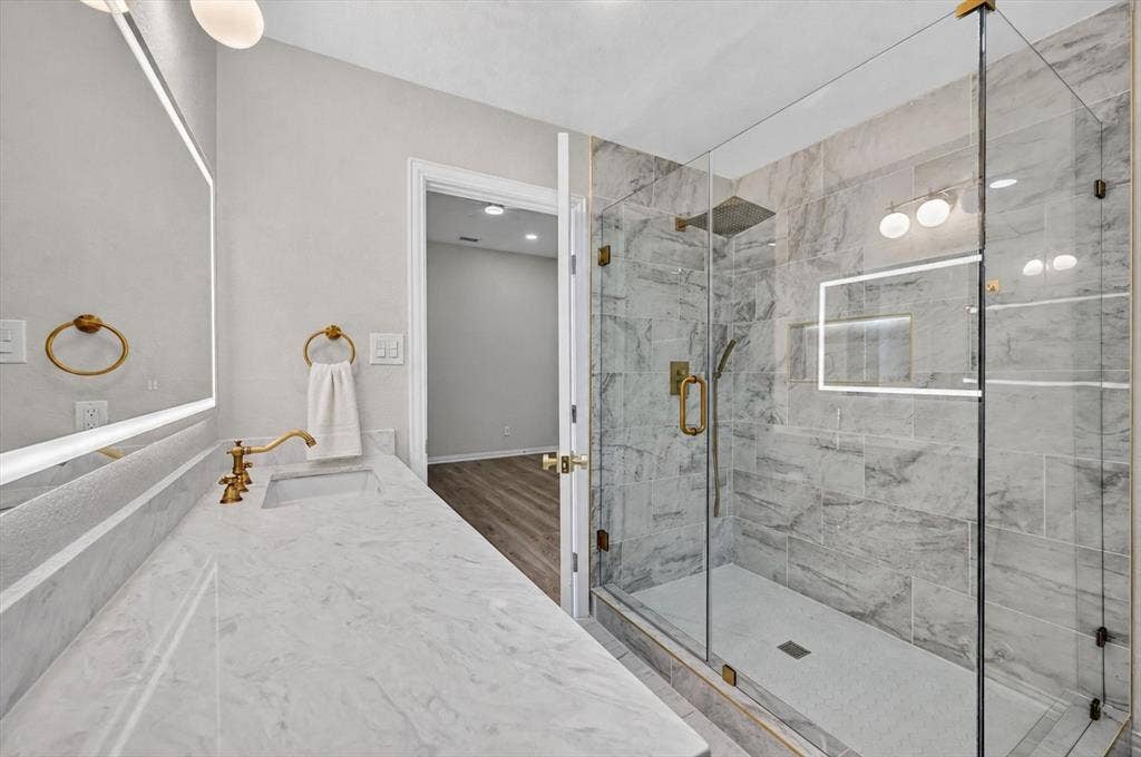 4437 Lone Tree Drive, Plano, TX 75093 Contemporary bathroom featuring a spacious glass-enclosed shower with gold-tone fixtures, a built-in shower niche, and large format wall tiling