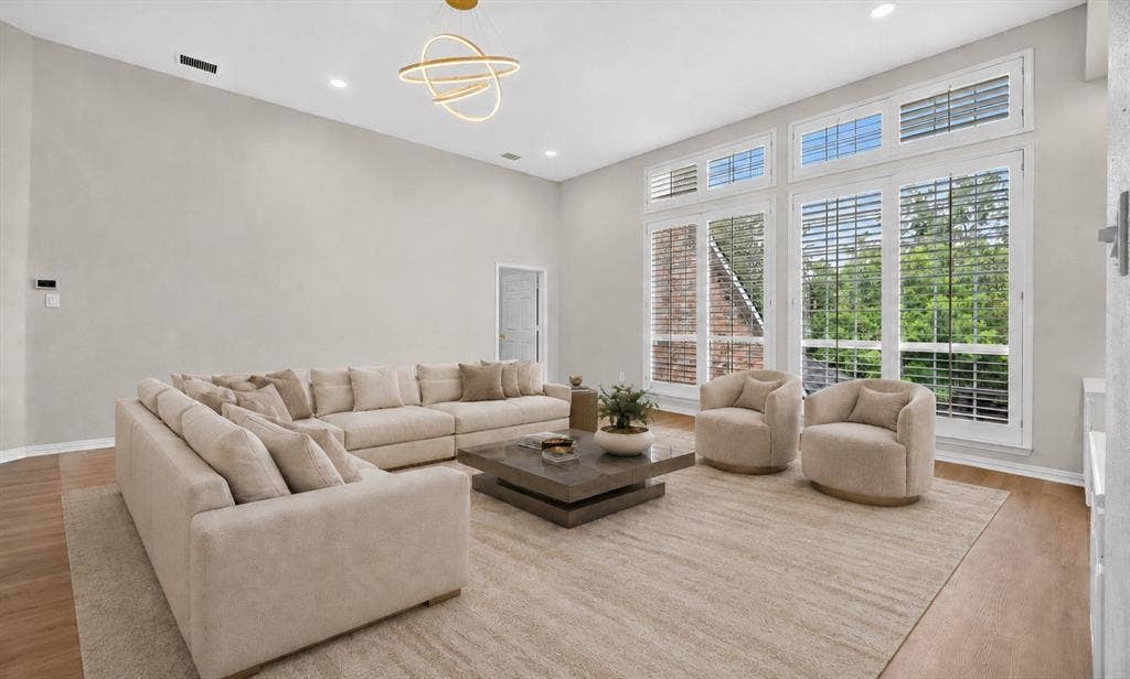 4437 Lone Tree Drive, Plano, TX 75093 Spacious living area featuring expansive windows with plantation shutters, vaulted ceilings, recessed lighting, and wood-finish flooring