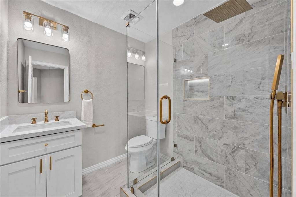 4437 Lone Tree Drive, Plano, TX 75093 Bathroom featuring a glass-enclosed shower with large-format stone-look tile, a built-in shower niche, and a gold-finish rainfall showerhead