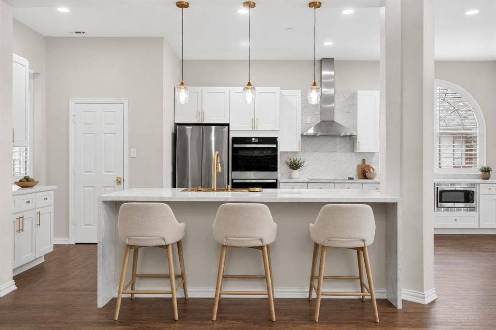 4437 Lone Tree Drive, Plano, TX 75093 Modern kitchen featuring a waterfall island with counter seating, stainless steel appliances, and white shaker cabinetry