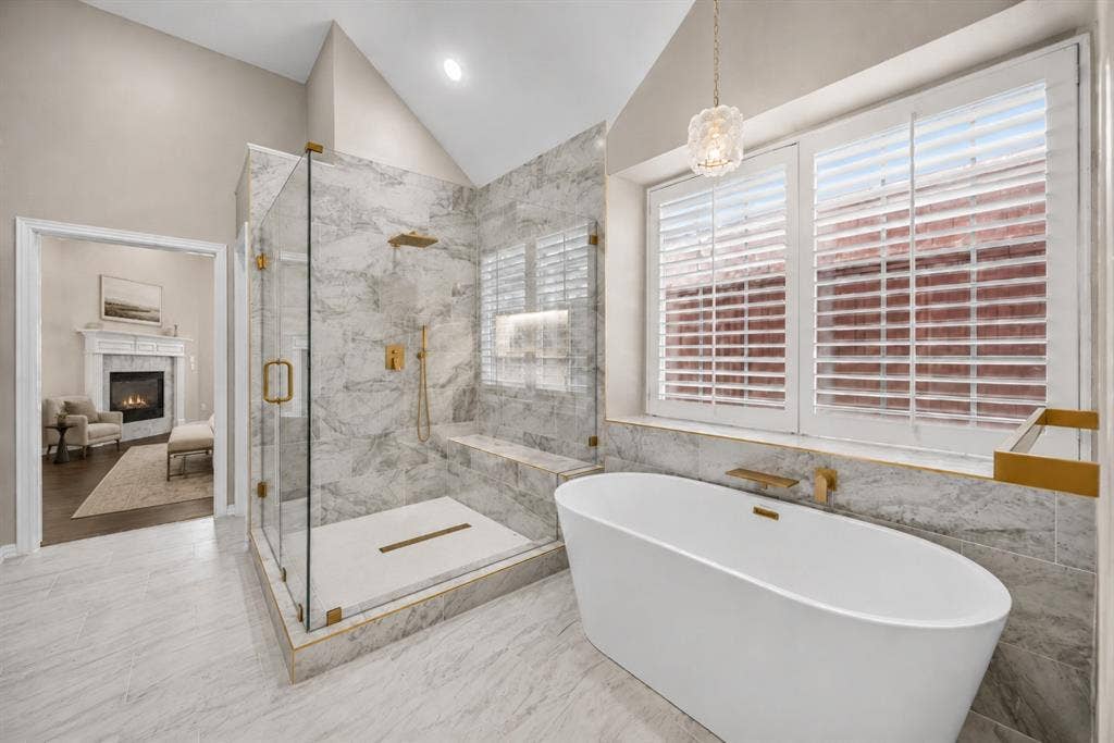 4437 Lone Tree Drive, Plano, TX 75093 Luxurious bathroom featuring a spacious walk-in shower with a built-in bench, a freestanding soaking tub with a wall-mounted faucet, plantation shutters, and a vaulted ceiling