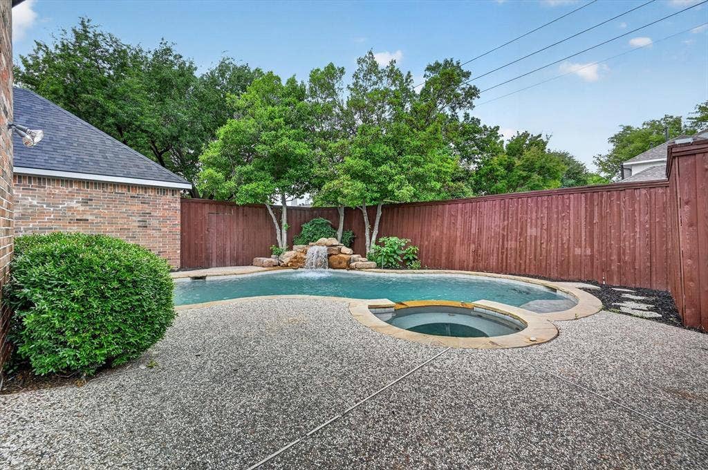 4437 Lone Tree Drive, Plano, TX 75093 Rear yard featuring a freeform swimming pool with rock waterfall, integrated spa, and exposed aggregate concrete decking