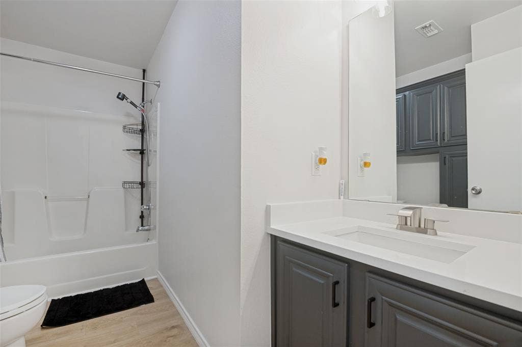 Bathroom featuring a white bathtub with shower, light wood-finish flooring, and a vanity with dark gray cabinetry, integrated sink, and brushed nickel faucet