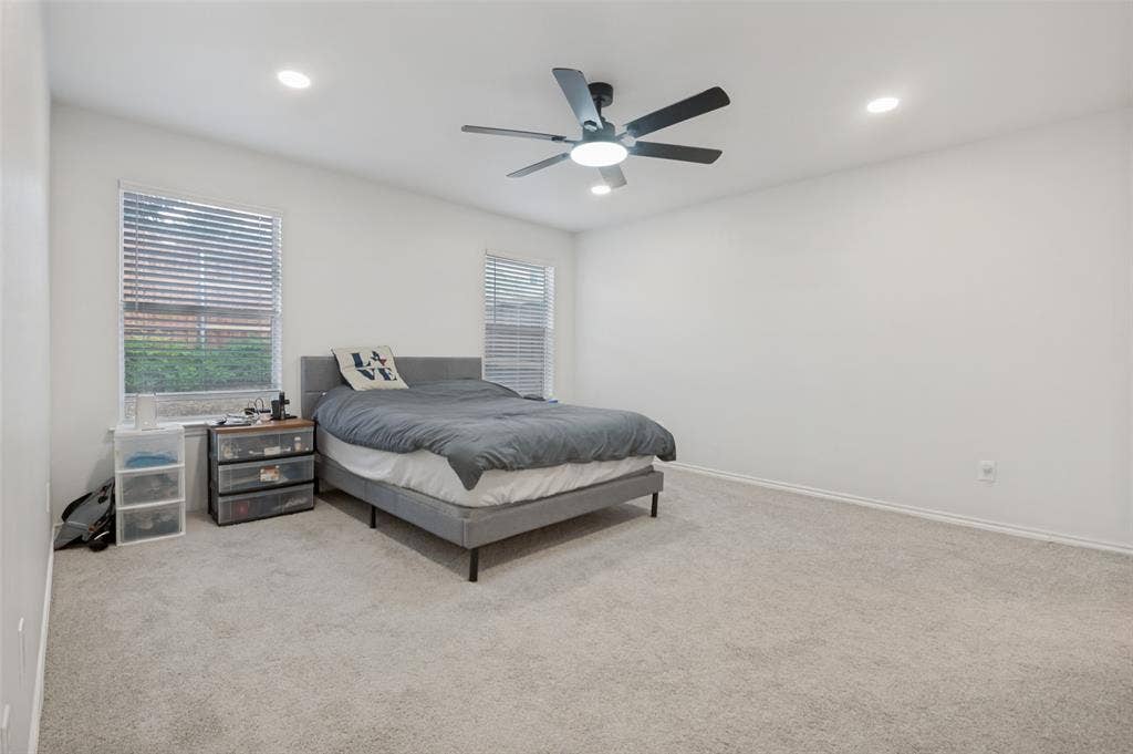 Carpeted room featuring two windows with horizontal blinds, recessed lighting, and a ceiling fan with integrated light