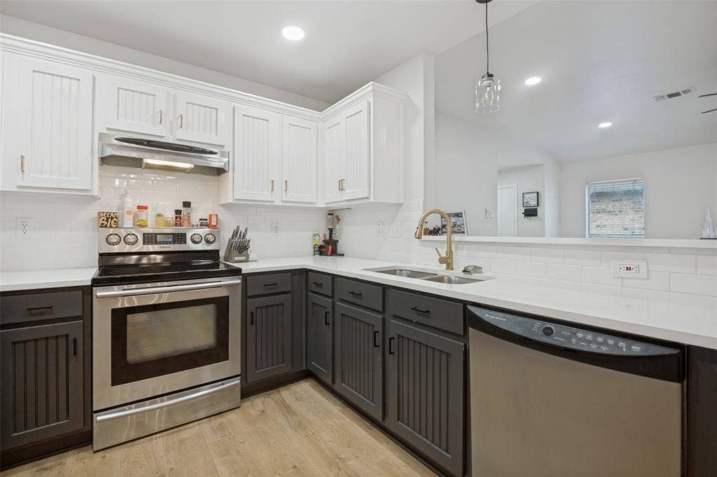 Contemporary kitchen featuring two-tone cabinetry, stainless steel appliances, a double basin sink with a brass-finish faucet, and recessed lighting