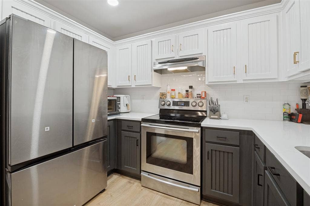 Contemporary kitchen featuring stainless steel appliances, two-tone cabinetry with beadboard detailing, white subway tile backsplash, and light wood-finish flooring