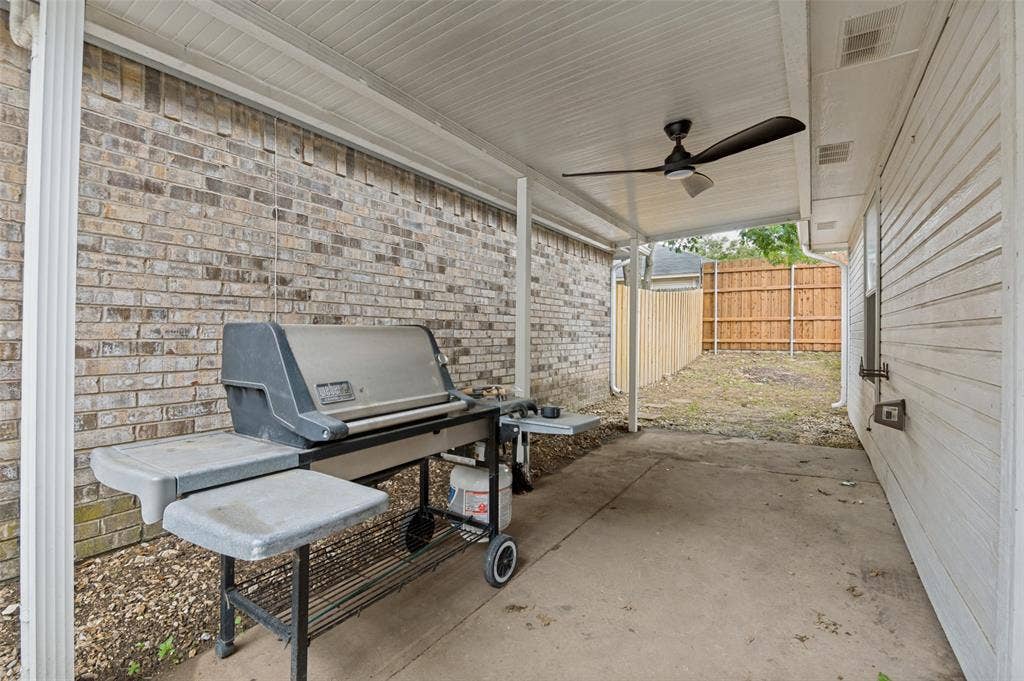 Covered concrete patio featuring a ceiling fan, a brick exterior wall, and a wood privacy fence