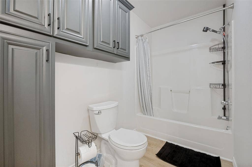 Bathroom featuring a white toilet, light wood-finish flooring, and a white tub-shower combination with a shower curtain rod