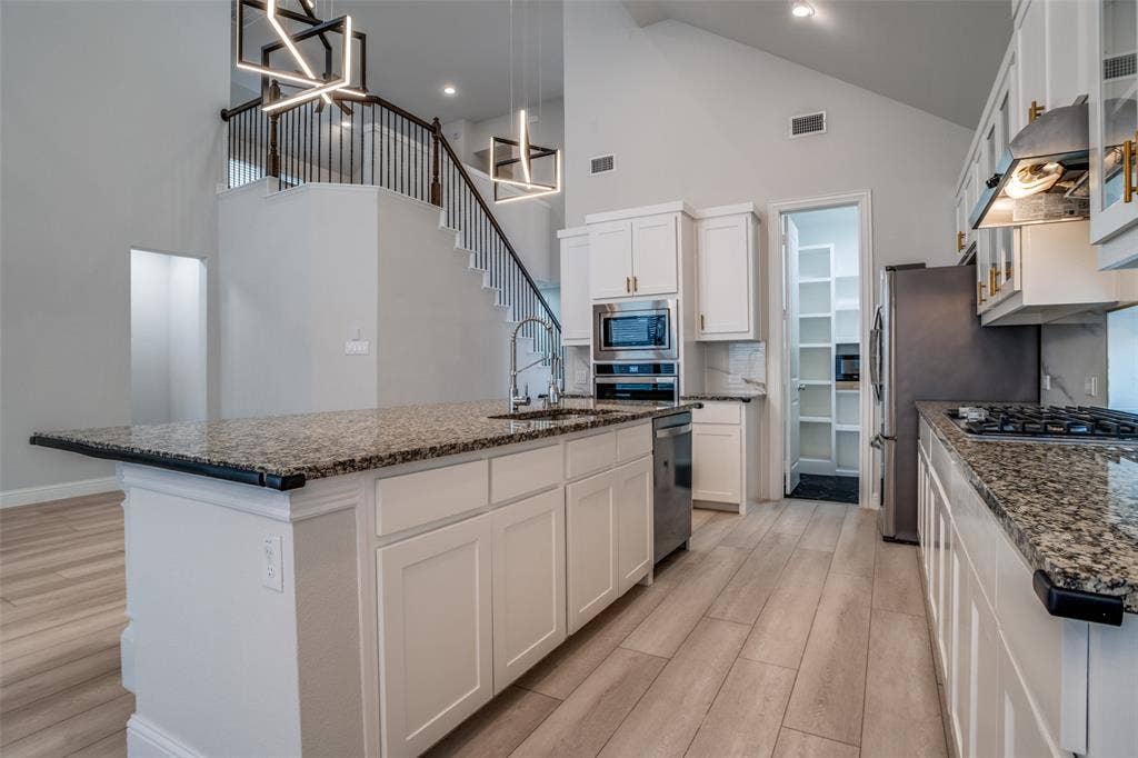 2811 Killdeer Trail, Prosper, TX 75078 Kitchen with white cabinets, a center island with sink, dark stone counters, light wood-style flooring, and lofted ceiling
