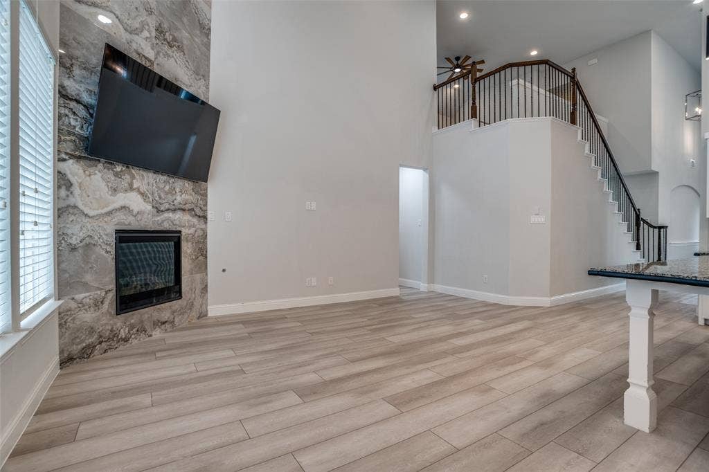 2811 Killdeer Trail, Prosper, TX 75078 Unfurnished living room featuring a ceiling fan, a glass covered fireplace, light wood-style floors, a high ceiling, and recessed lighting