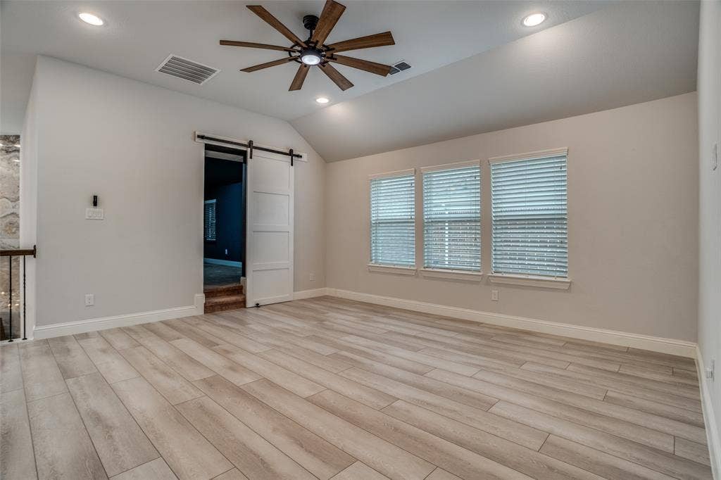 2811 Killdeer Trail, Prosper, TX 75078 Unfurnished bedroom featuring a barn door, recessed lighting, light wood-type flooring, a ceiling fan, and vaulted ceiling