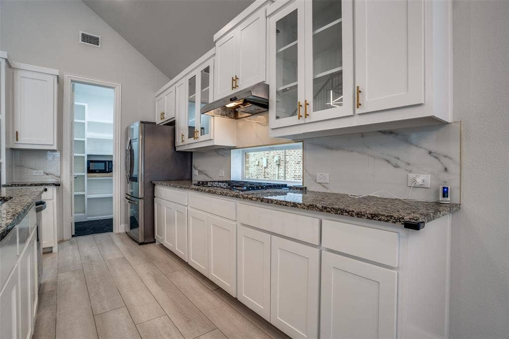 2811 Killdeer Trail, Prosper, TX 75078 Kitchen featuring lofted ceiling, white cabinetry, glass insert cabinets, light wood-type flooring, and dark stone countertops