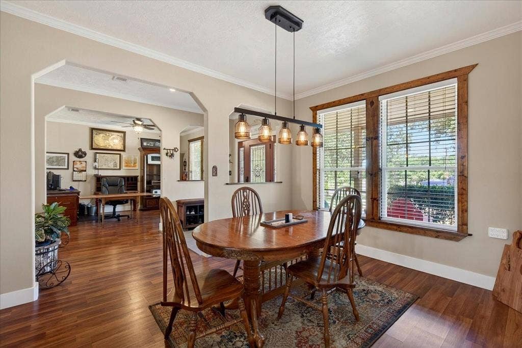 11591 Fm 59, Athens, TX 75751 Dining area featuring wood-finish flooring, a linear pendant light fixture with amber glass shades, and two windows framed with natural wood trim, open to living-office-kitchen.