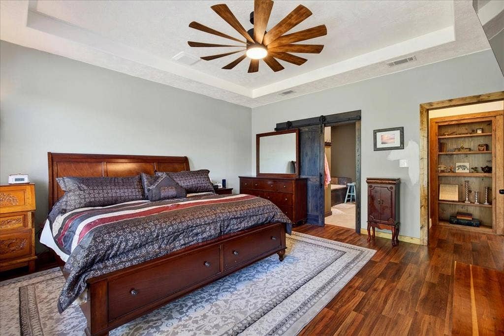 11591 Fm 59, Athens, TX 75751 Primary Bedroom featuring wood-finish flooring, a tray ceiling with a farm-style ceiling fan, and a barn door entry