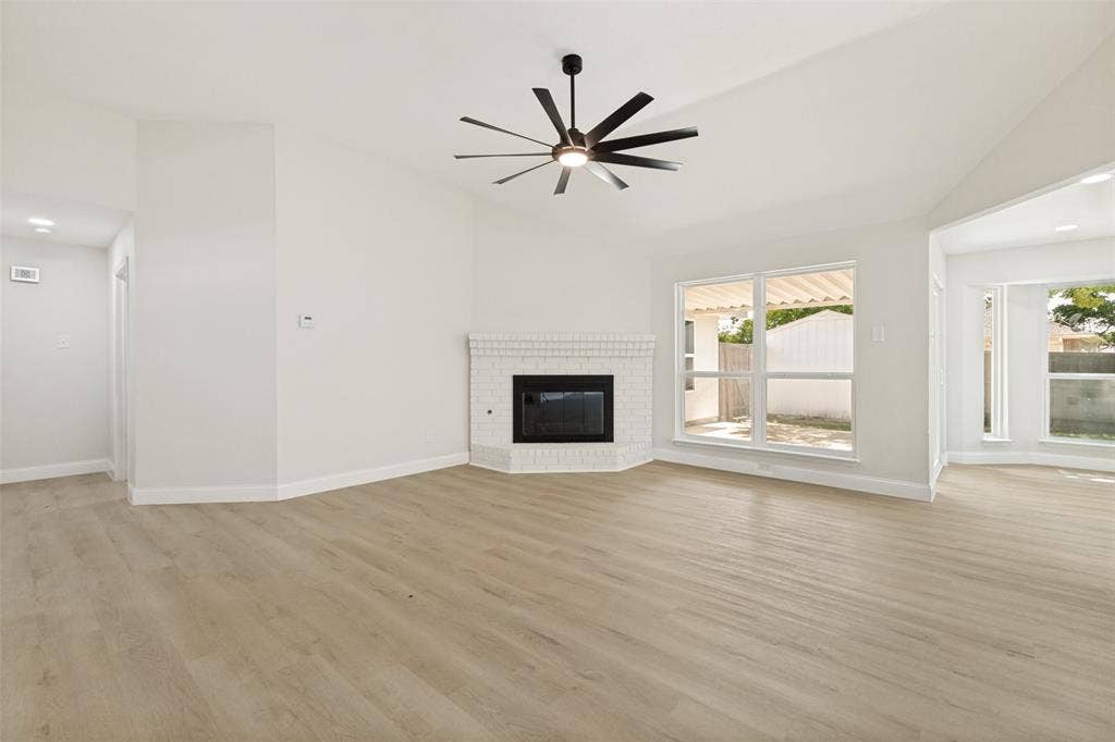 713 Bridgewater Lane, Mesquite, TX 75181 Spacious living area featuring vaulted ceilings, wood-finish flooring, a white brick fireplace, a modern ceiling fan, and multiple large windows