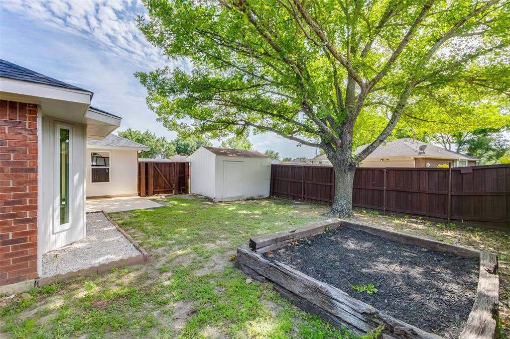 713 Bridgewater Lane, Mesquite, TX 75181 Spacious backyard featuring a substantial tree providing natural shade, a raised garden bed, a white storage shed, and a privacy fence