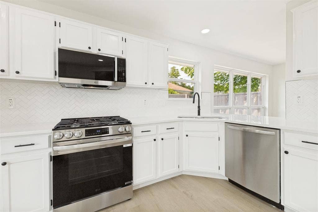 713 Bridgewater Lane, Mesquite, TX 75181 Modern kitchen featuring white cabinetry, stainless steel appliances, a white herringbone tile backsplash, light wood-finish flooring, and white countertops