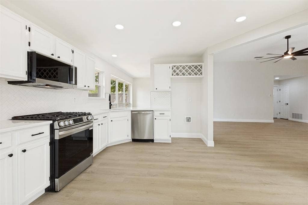 713 Bridgewater Lane, Mesquite, TX 75181 Bright kitchen featuring white cabinetry, stainless steel appliances, light-toned wood-finish flooring, recessed lighting, and an integrated wine rack