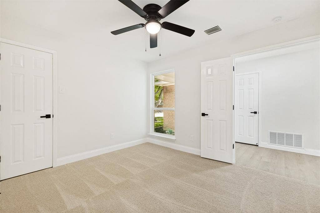 713 Bridgewater Lane, Mesquite, TX 75181 Spacious room featuring neutral paint, light-colored carpet, a ceiling fan with integrated lighting, a large window, and multiple panel doors with matte black hardware