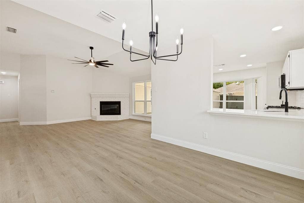 713 Bridgewater Lane, Mesquite, TX 75181 Open-concept living space featuring wood-finish flooring, a contemporary black chandelier, a corner fireplace with a white brick surround, vaulted ceilings, and a kitchen pass-through with a white countertop