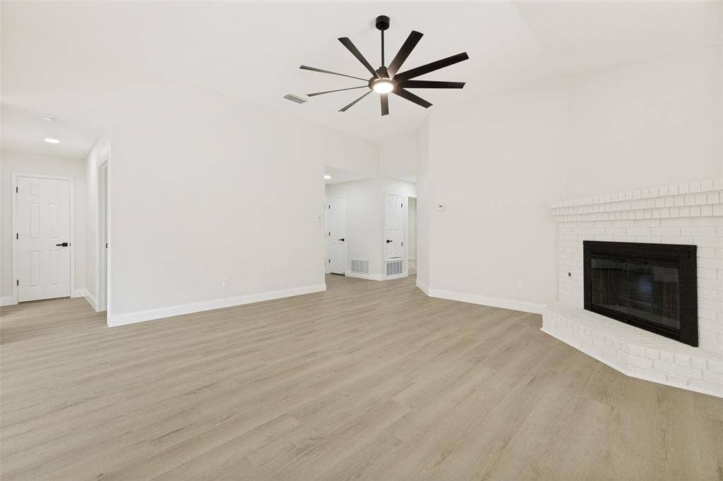713 Bridgewater Lane, Mesquite, TX 75181 Spacious room featuring vaulted ceilings, wood-finish flooring, a modern ceiling fan with integrated lighting, and a white brick fireplace
