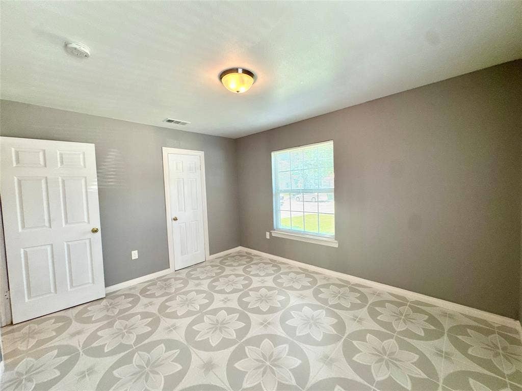 Room featuring patterned flooring, neutral gray walls, a window with white trim, and two white paneled doors