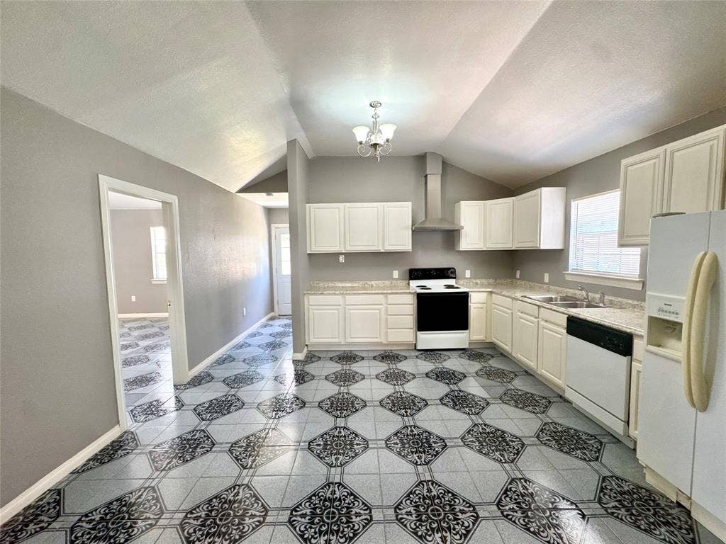 Spacious kitchen featuring patterned tile flooring, white cabinetry, light countertops, and a modern stainless steel range hood
