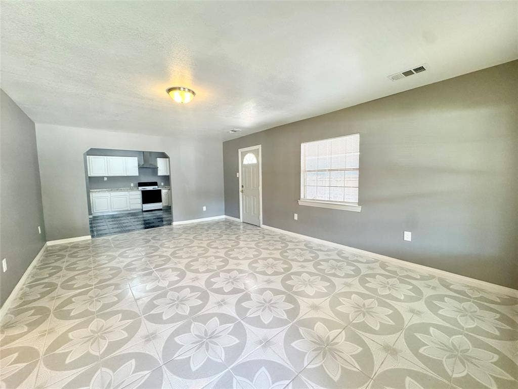 Spacious living area featuring patterned floor tiling, neutral gray walls, a ceiling-mounted light fixture, and a window with blinds
