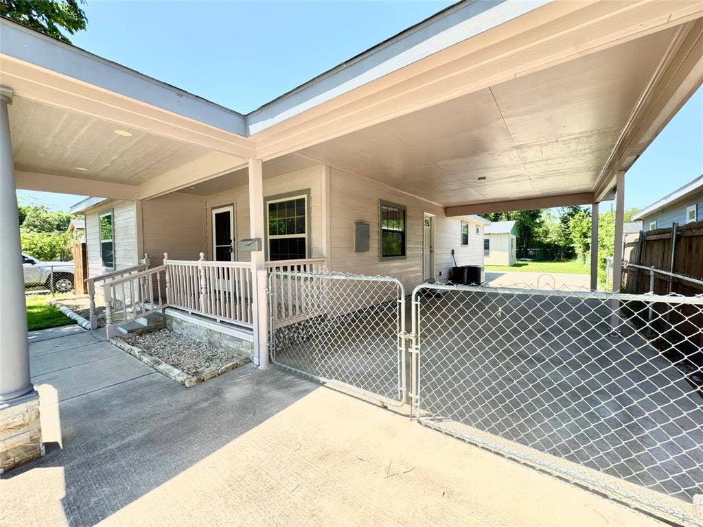 Covered carport entrance featuring a concrete driveway, chain-link fencing, a covered porch with railings, and exterior siding