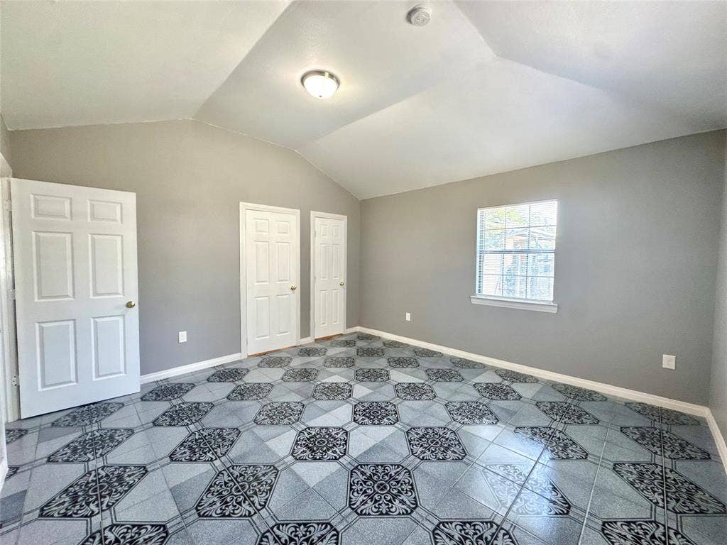 Room featuring a vaulted ceiling and patterned tile flooring