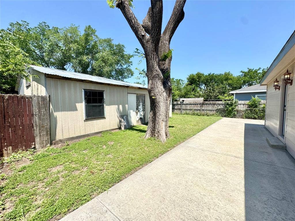 Expansive concrete patio alongside a detached storage shed with a metal roof and painted siding