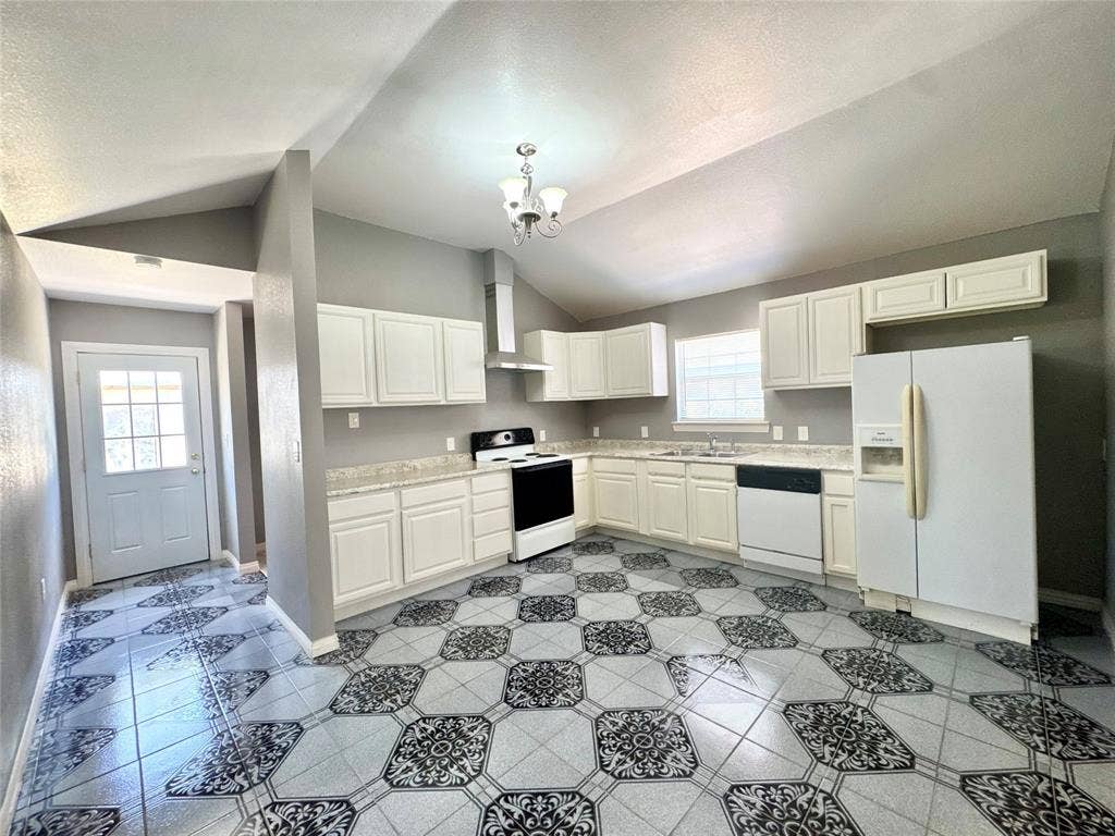 Kitchen featuring vaulted ceilings, white cabinetry, light-toned countertops, a full suite of white appliances, and patterned floor tiling