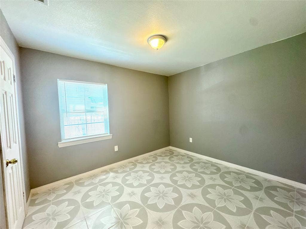 Neutral-toned room featuring patterned tile flooring, a window with horizontal blinds, and a flush-mount ceiling light fixture
