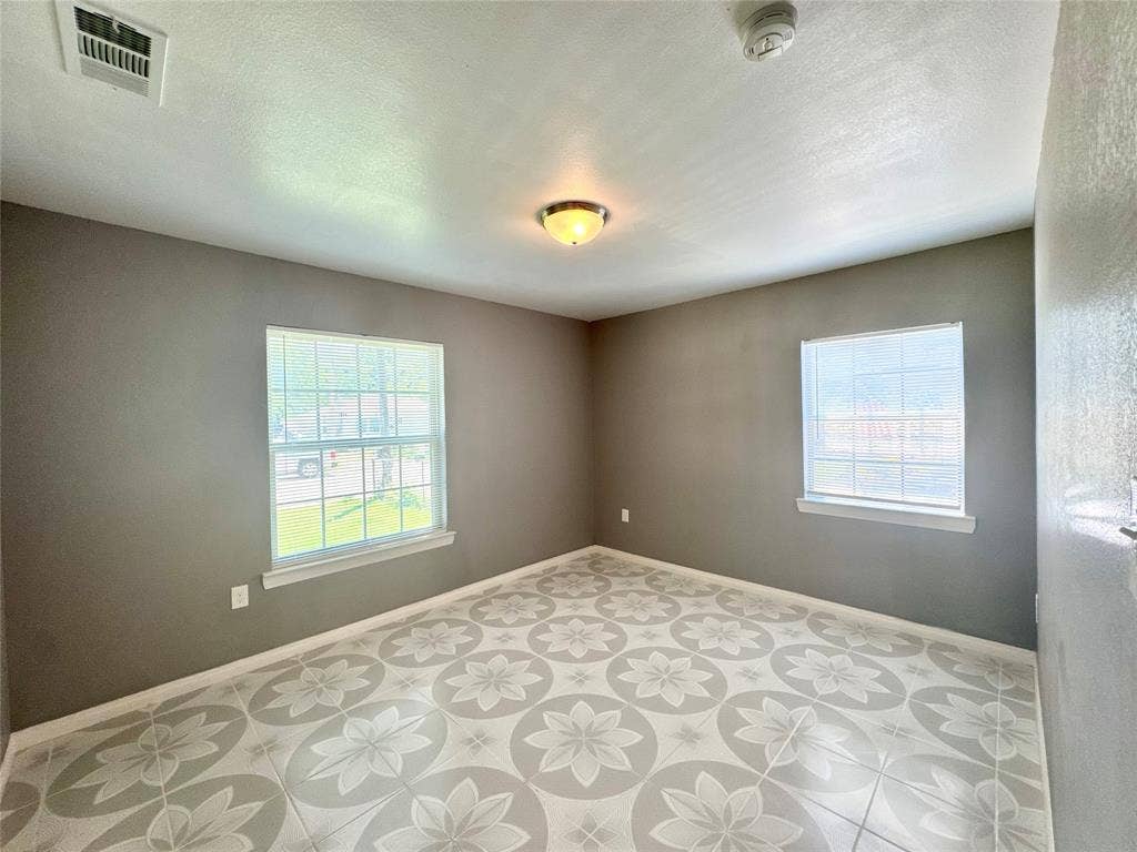 Spacious interior room featuring decorative floor tiling, two windows, a ceiling-mounted light fixture, and neutral painted walls