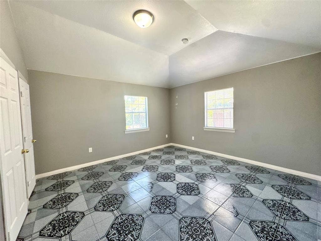 Vaulted ceiling room featuring patterned tile flooring, neutral wall paint, two windows, and bi-fold closet doors